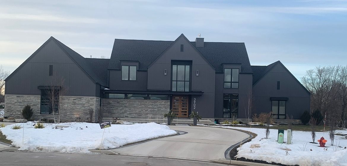 A large black house with a snowy driveway in front of it.