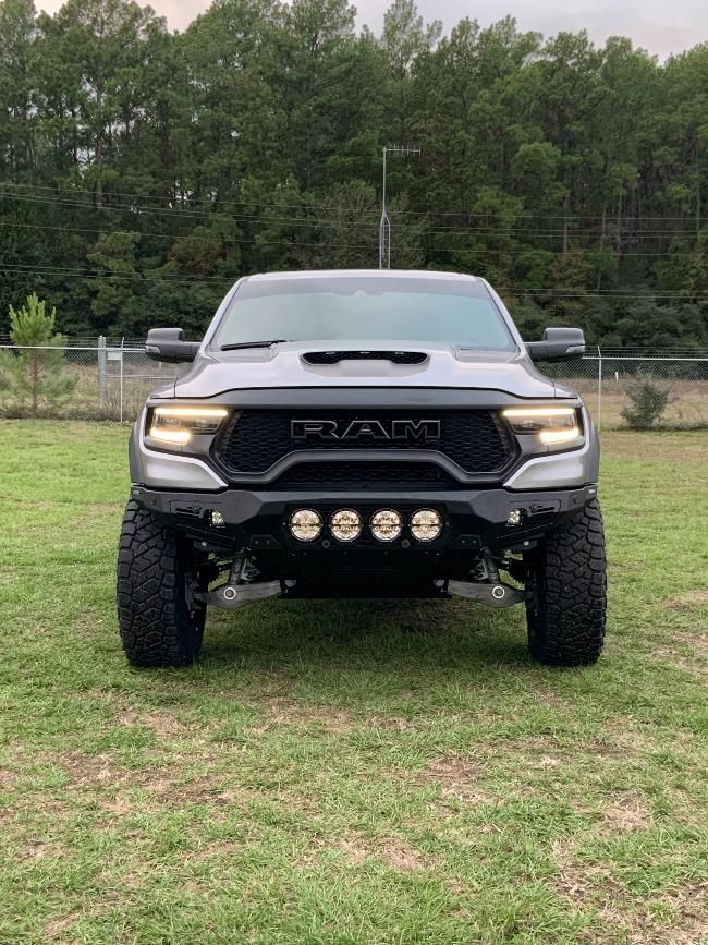 A ram truck is parked in a grassy field with trees in the background.