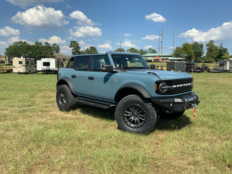 A blue ford bronco is parked in a grassy field.