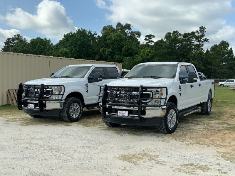 Two white trucks are parked next to each other in a gravel lot.