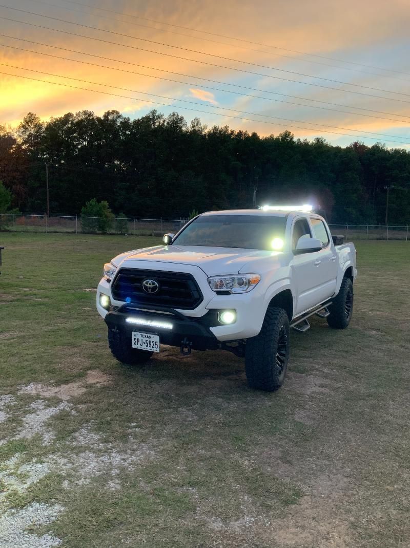 A white toyota tacoma truck is parked in a field at sunset.