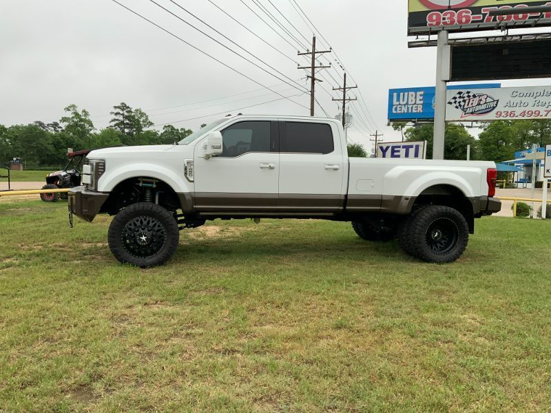 A white truck is parked in a grassy field in front of a billboard.