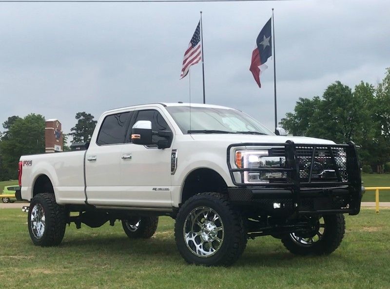 A white truck is parked in a grassy field with flags in the background.