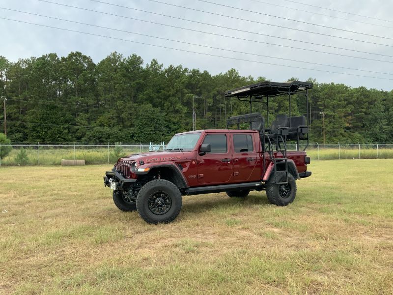 A red jeep with a golf cart attached to it is parked in a grassy field.