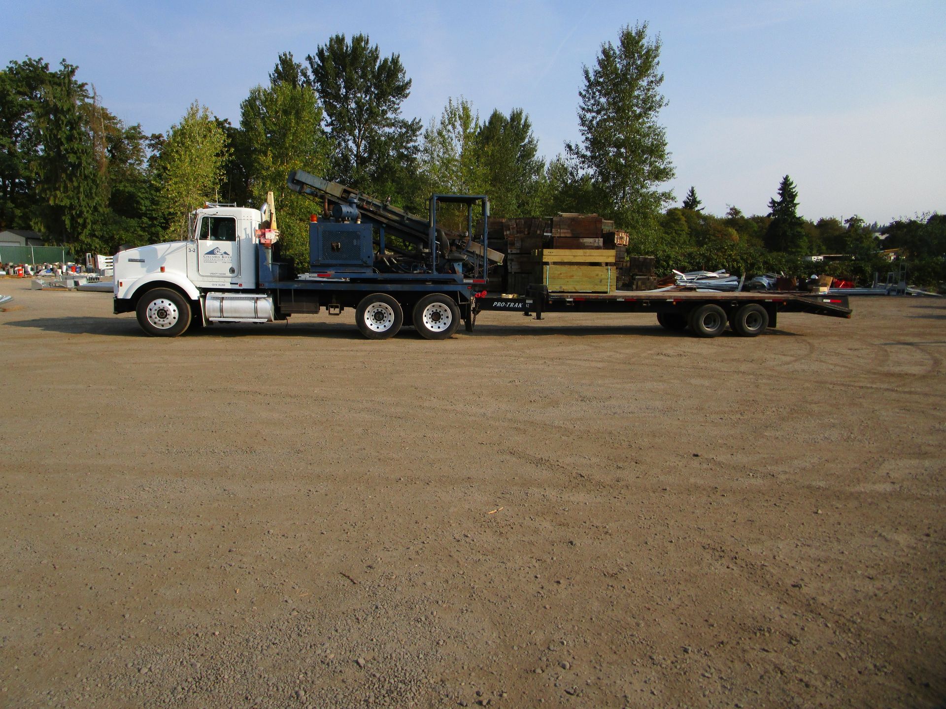 A semi truck with a flatbed trailer is parked in a dirt lot
