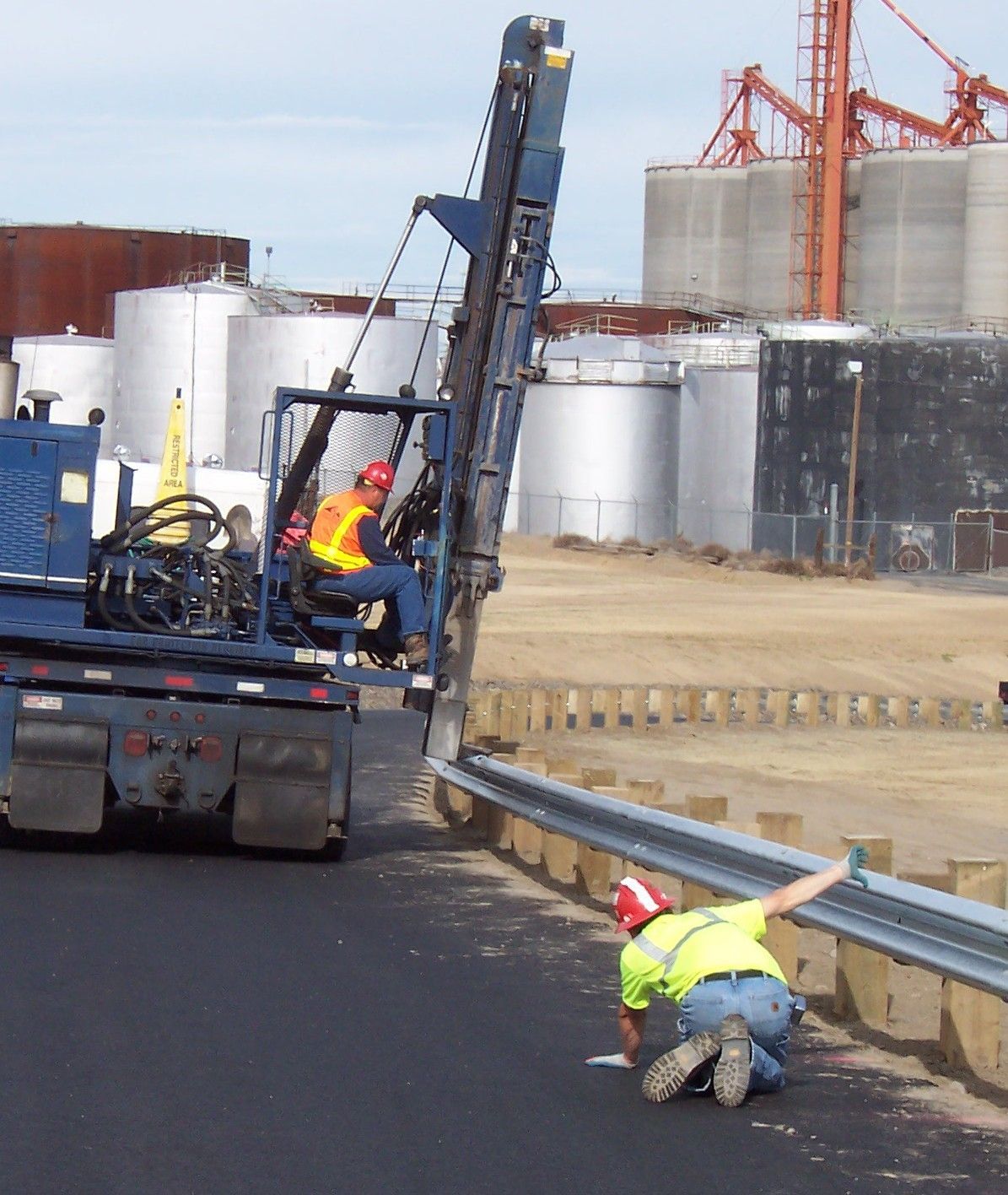 A man in a yellow vest is kneeling next to a blue truck