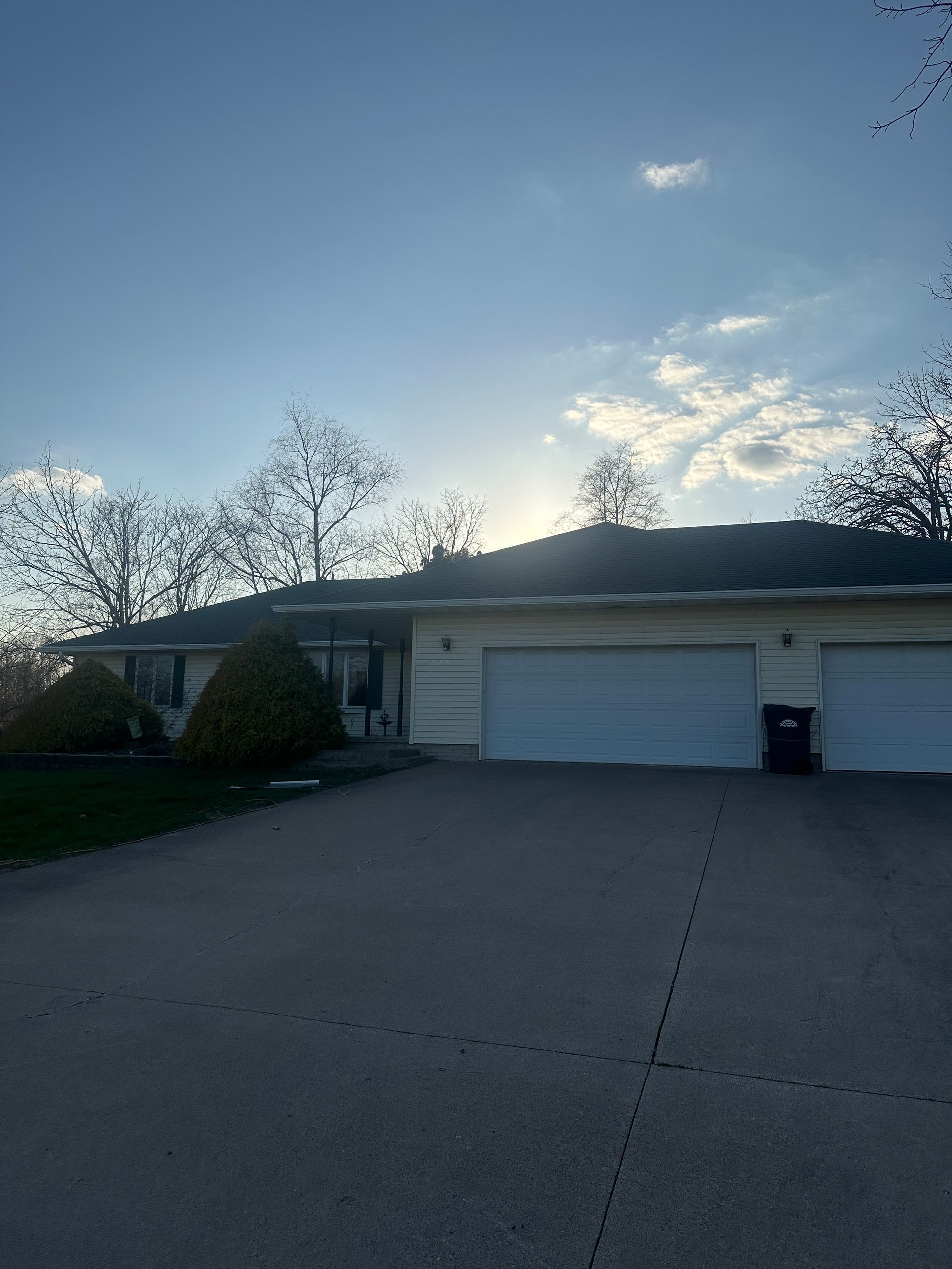 A light-colored house with a two-car garage under a sunny blue sky, viewed from a wide concrete driveway.