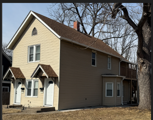 Two-story beige house with brown roof and white trim beside leafless trees