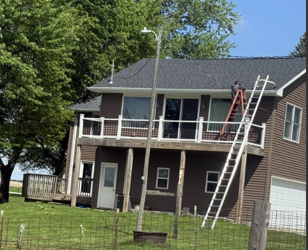 House with two-story porch and ladder; person on the roof repairing the shingles.