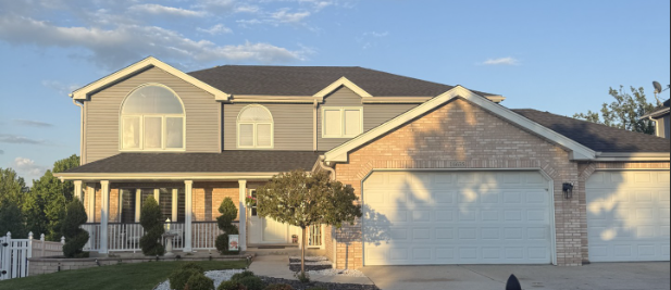 Two-story beige suburban house with a white garage and front porch at sunset