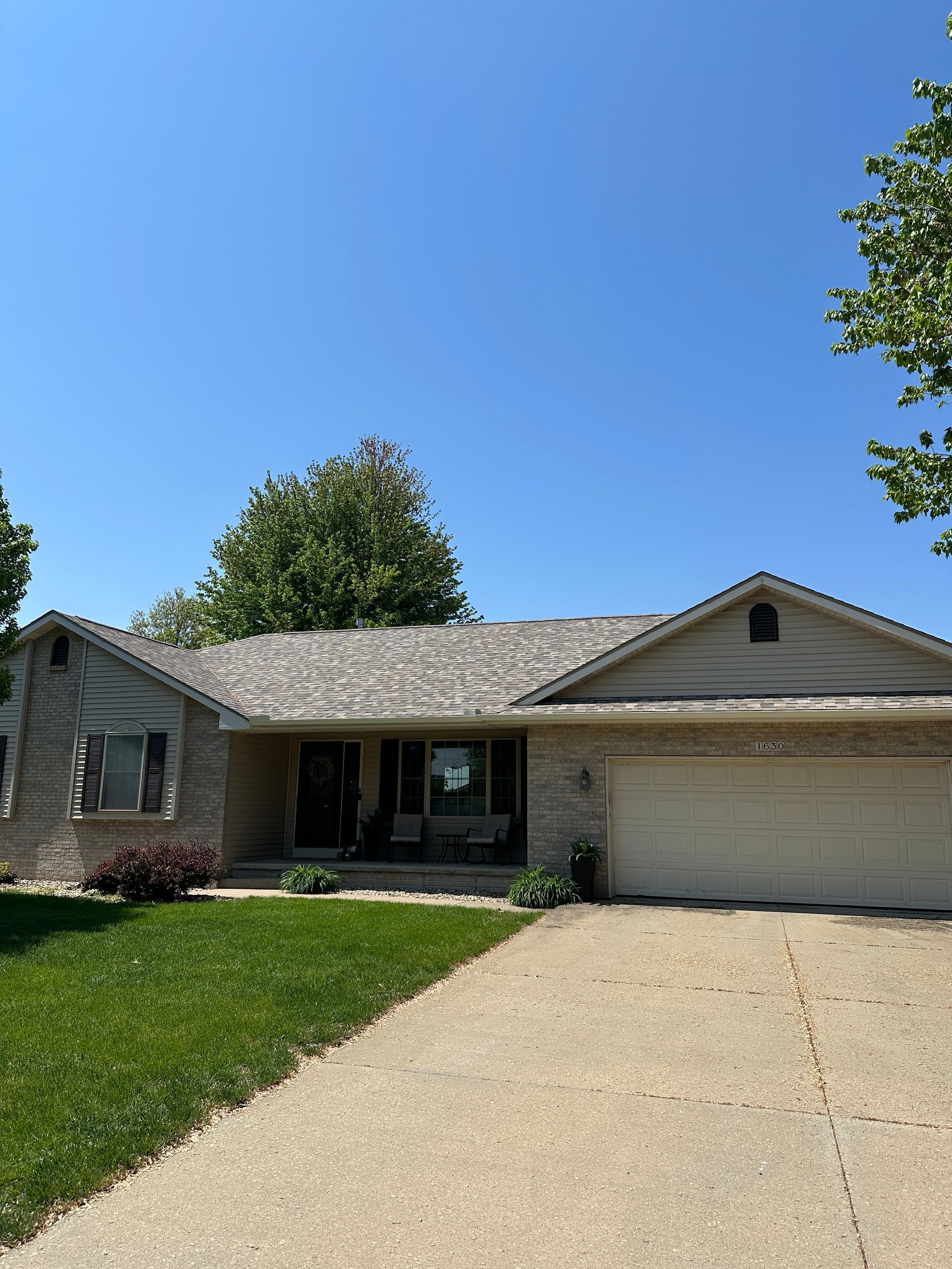 Single-story brick house with a beige garage and driveway under a clear blue sky on a sunny day.