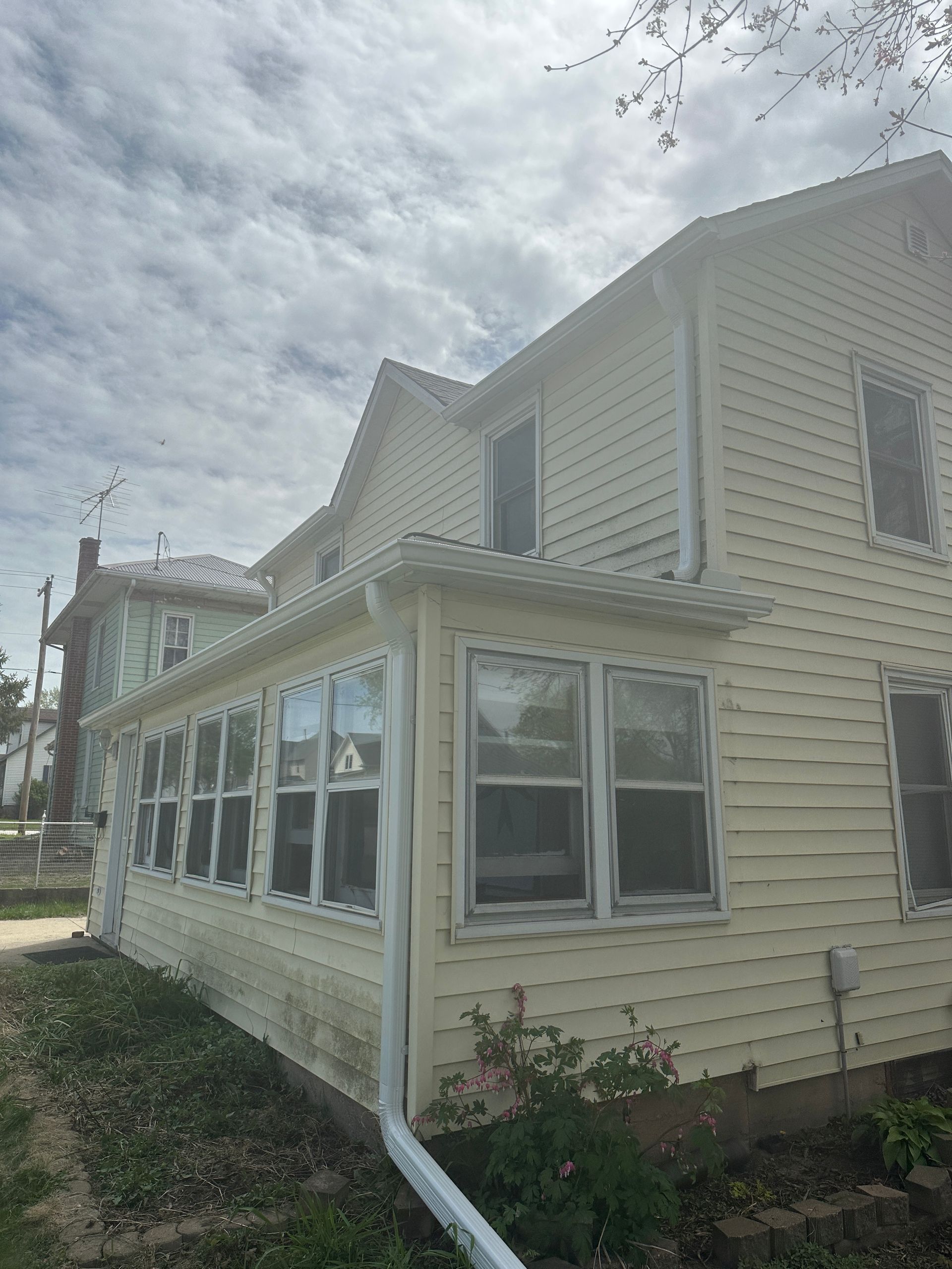 A light yellow two-story house with a white-enclosed porch under a cloudy sky.