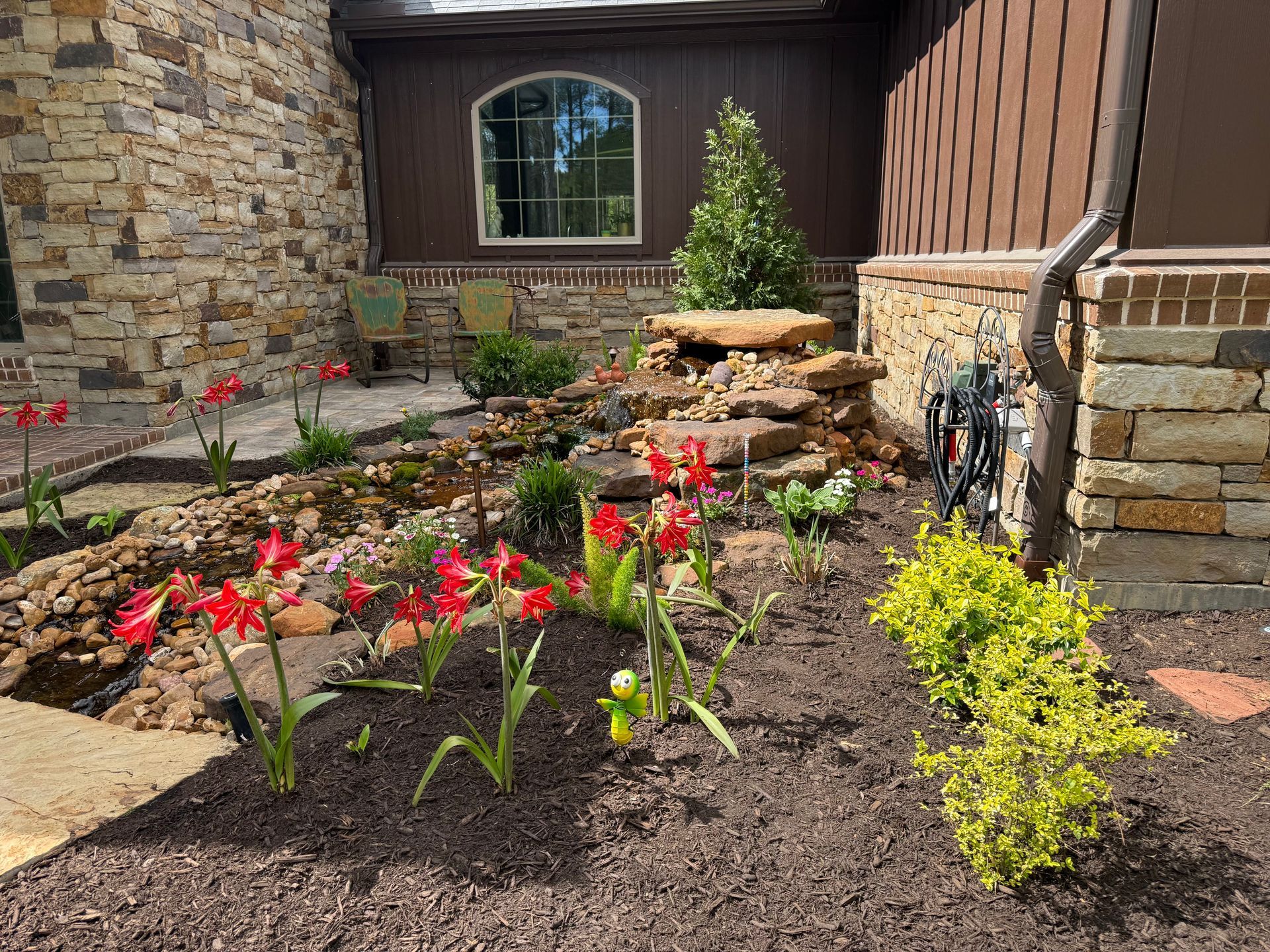 Flower bed with red tulips and a small stone fountain in a landscaped courtyard by stone and wood walls