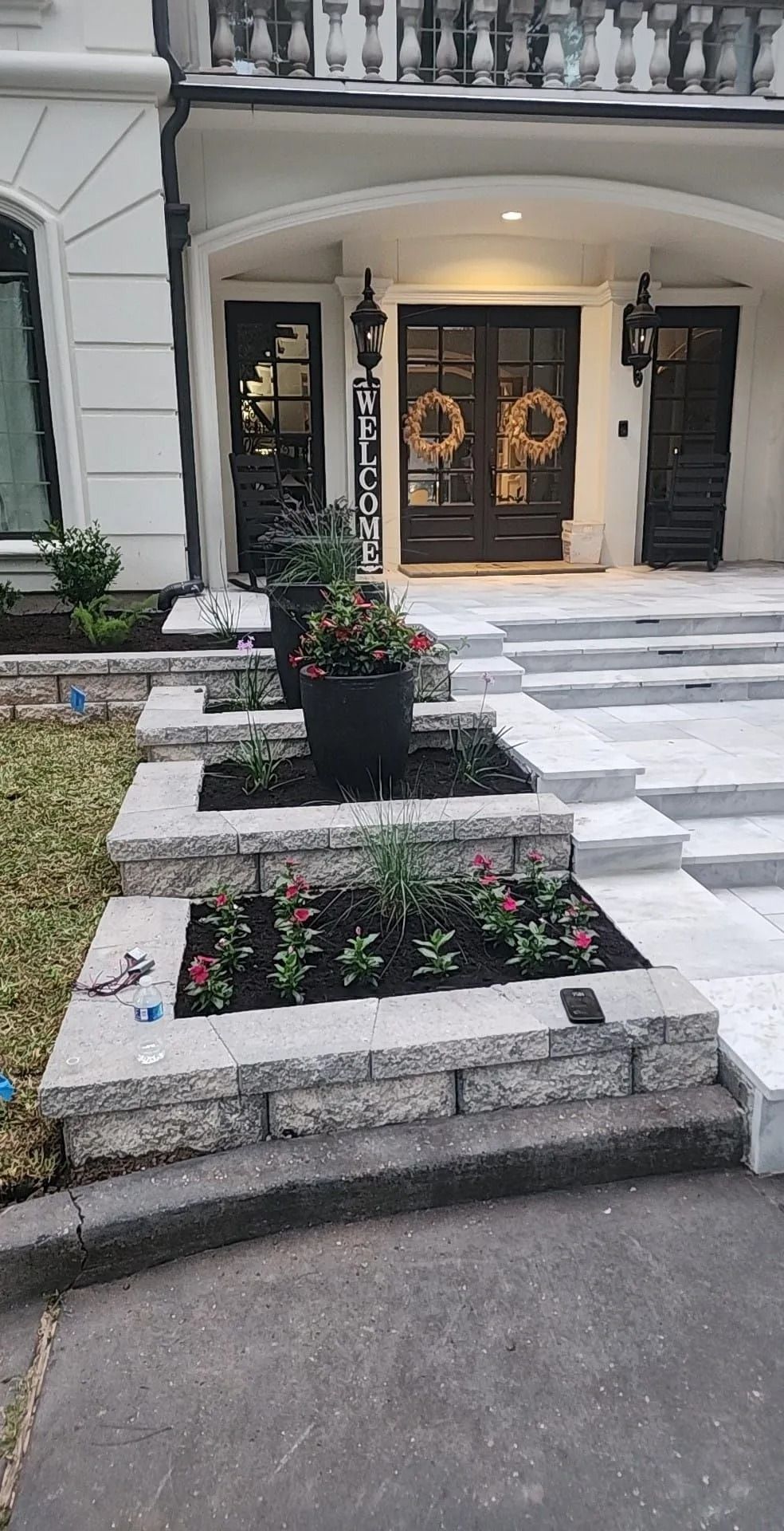 Front exterior of a home with steps and planters. Black door with wreaths, white trim, and stone retaining walls.