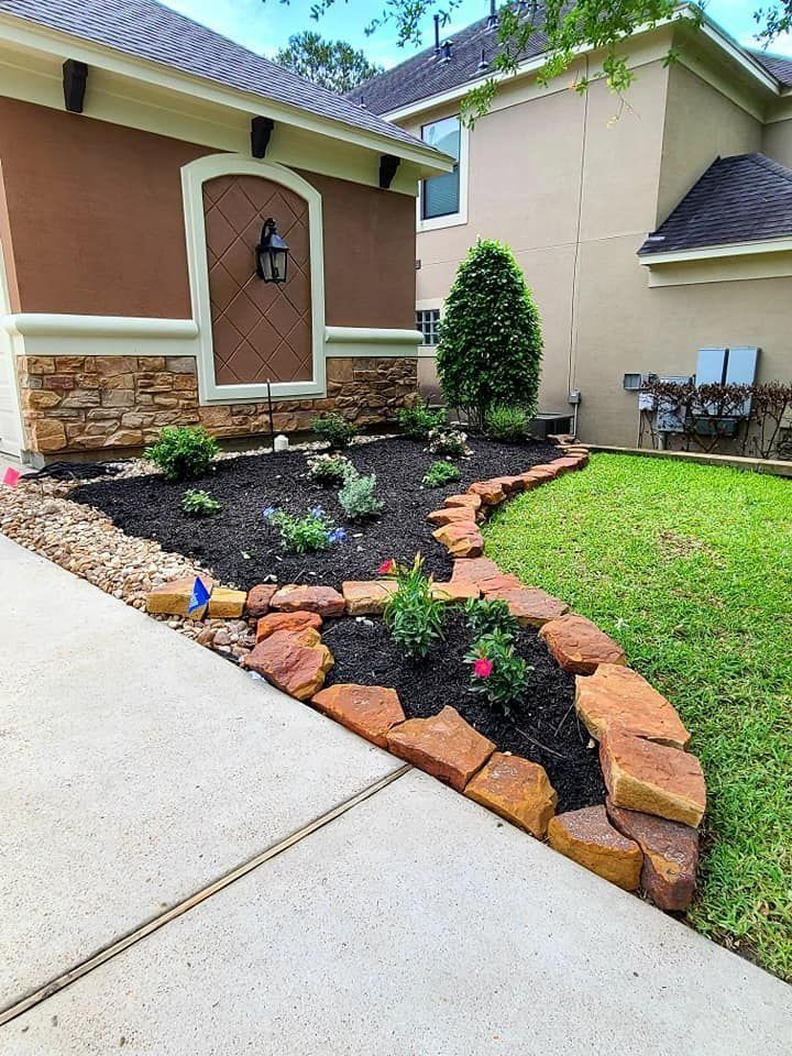 Landscaped flower bed with red brick border next to a driveway and house with beige and brown facade.