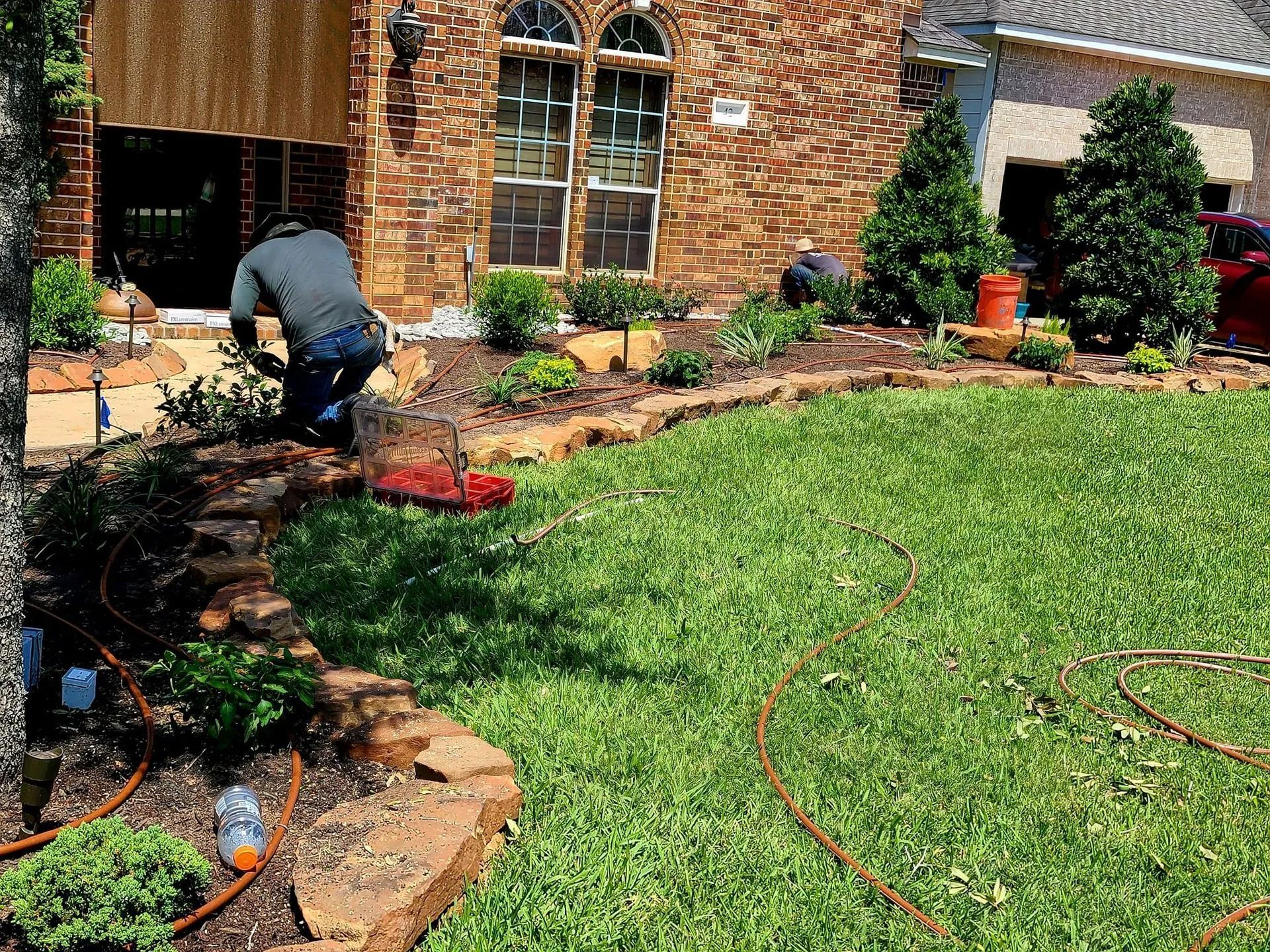 Landscapers working on a front yard with brick edging and green grass.