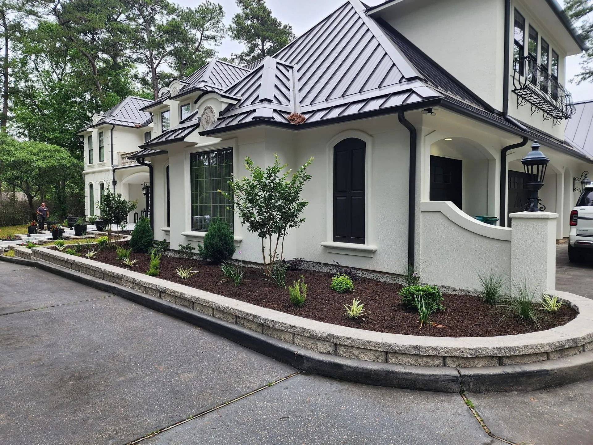 White stucco house with metal roof, landscaped border, and driveway.