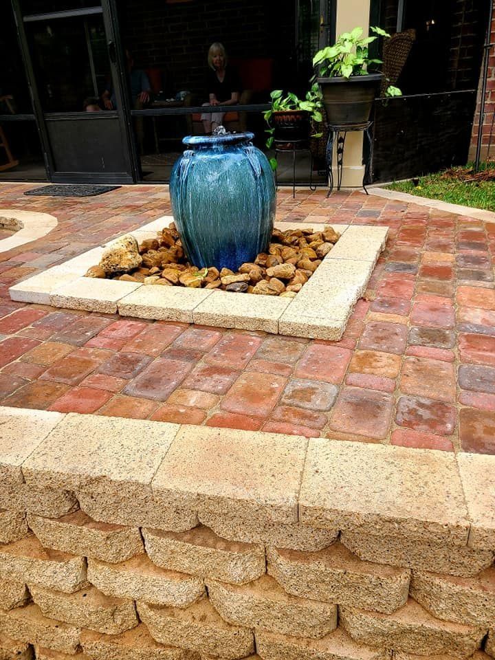 Outdoor fountain with blue glazed urn surrounded by rocks, on a brick patio.