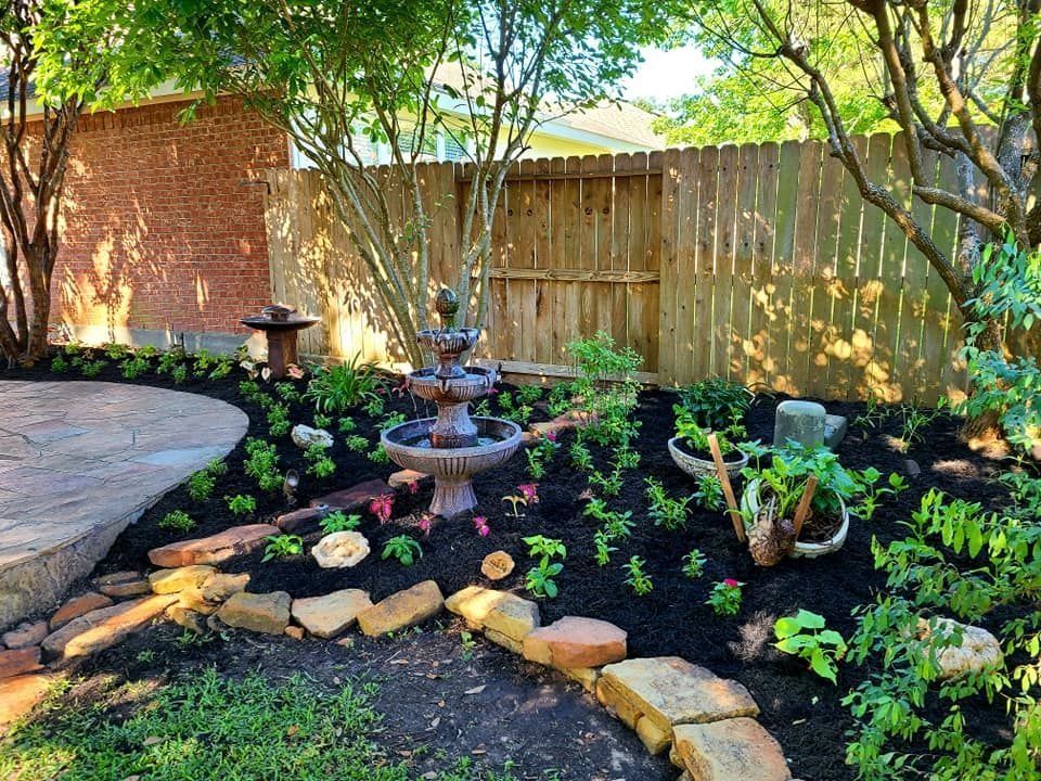 Landscaped backyard with fountain, stone edging, brick wall, wooden fence, and lush greenery.