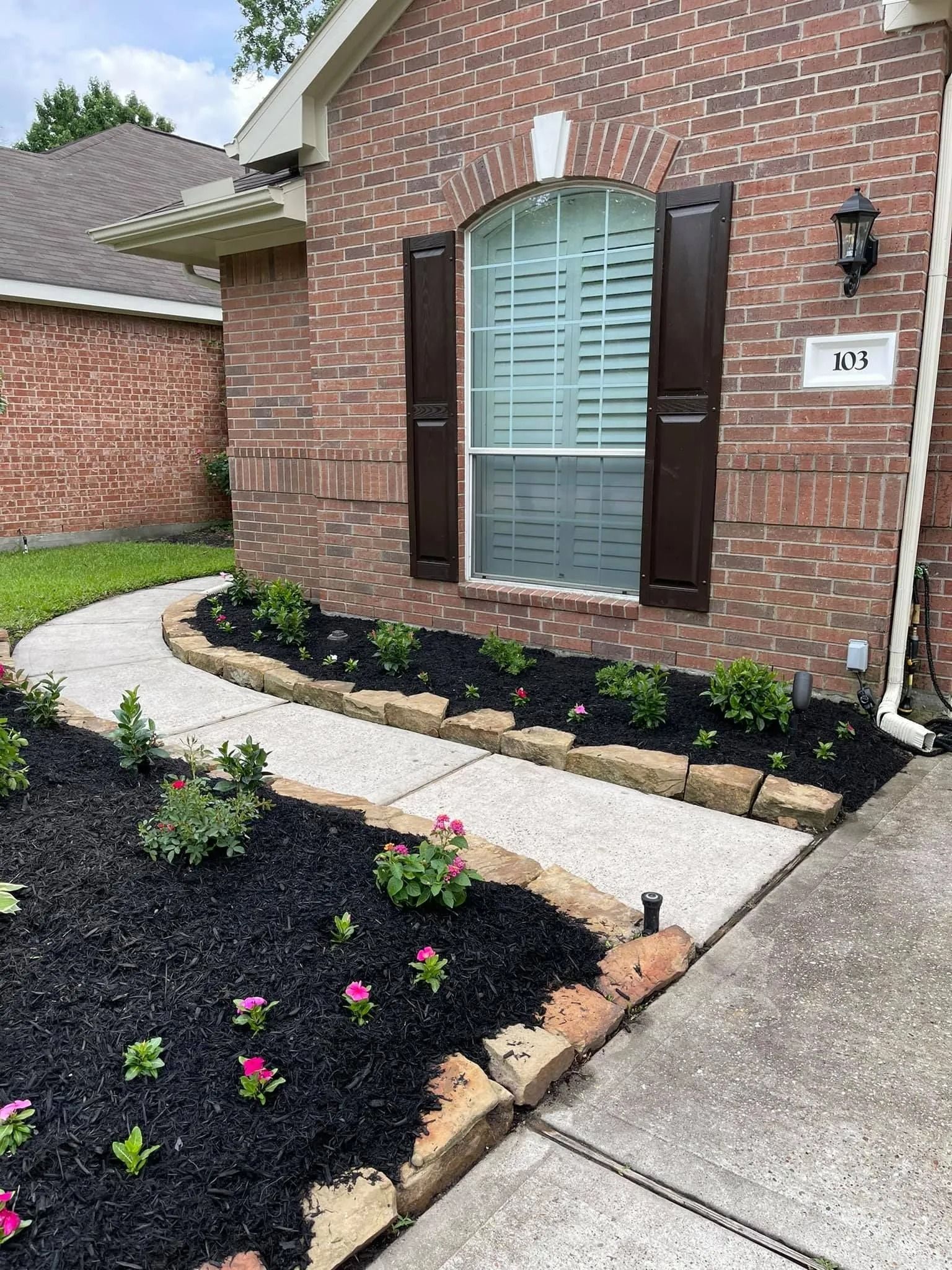 Brick home with a curved sidewalk, flower beds with pink flowers, and dark mulch.