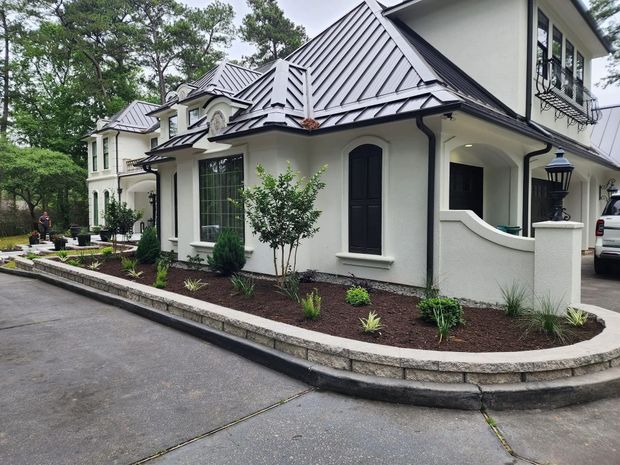 White stucco house with metal roof, landscaped border along driveway.