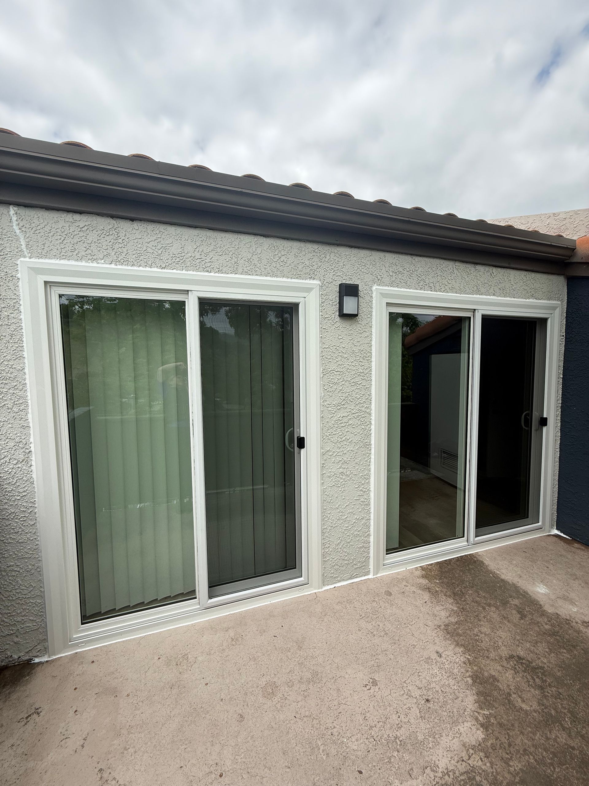 White patio doors and windows on a stucco house, with one sliding door open to the outside.
