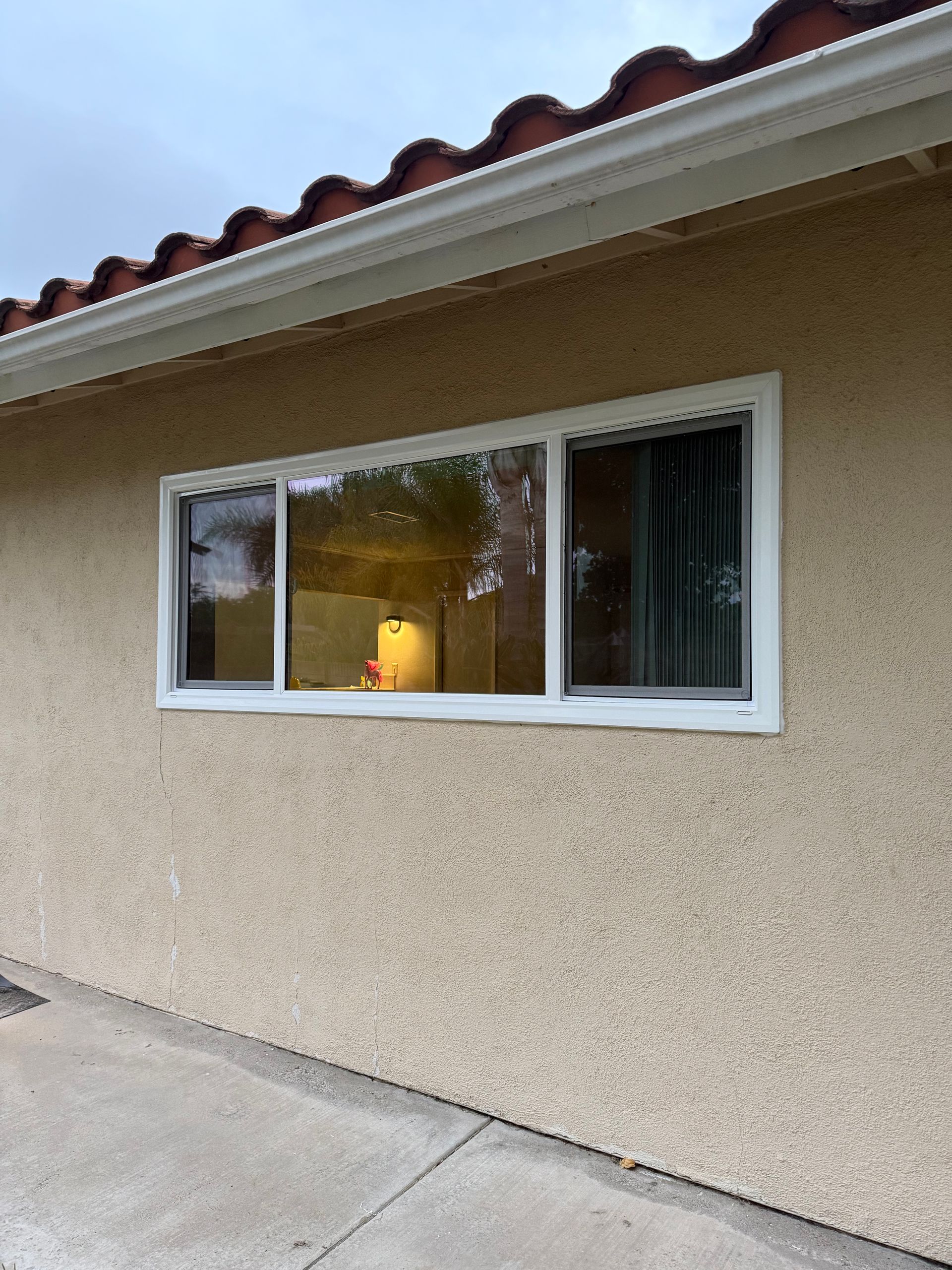 Exterior window on beige stucco wall with white trim and a small lamp glowing inside
