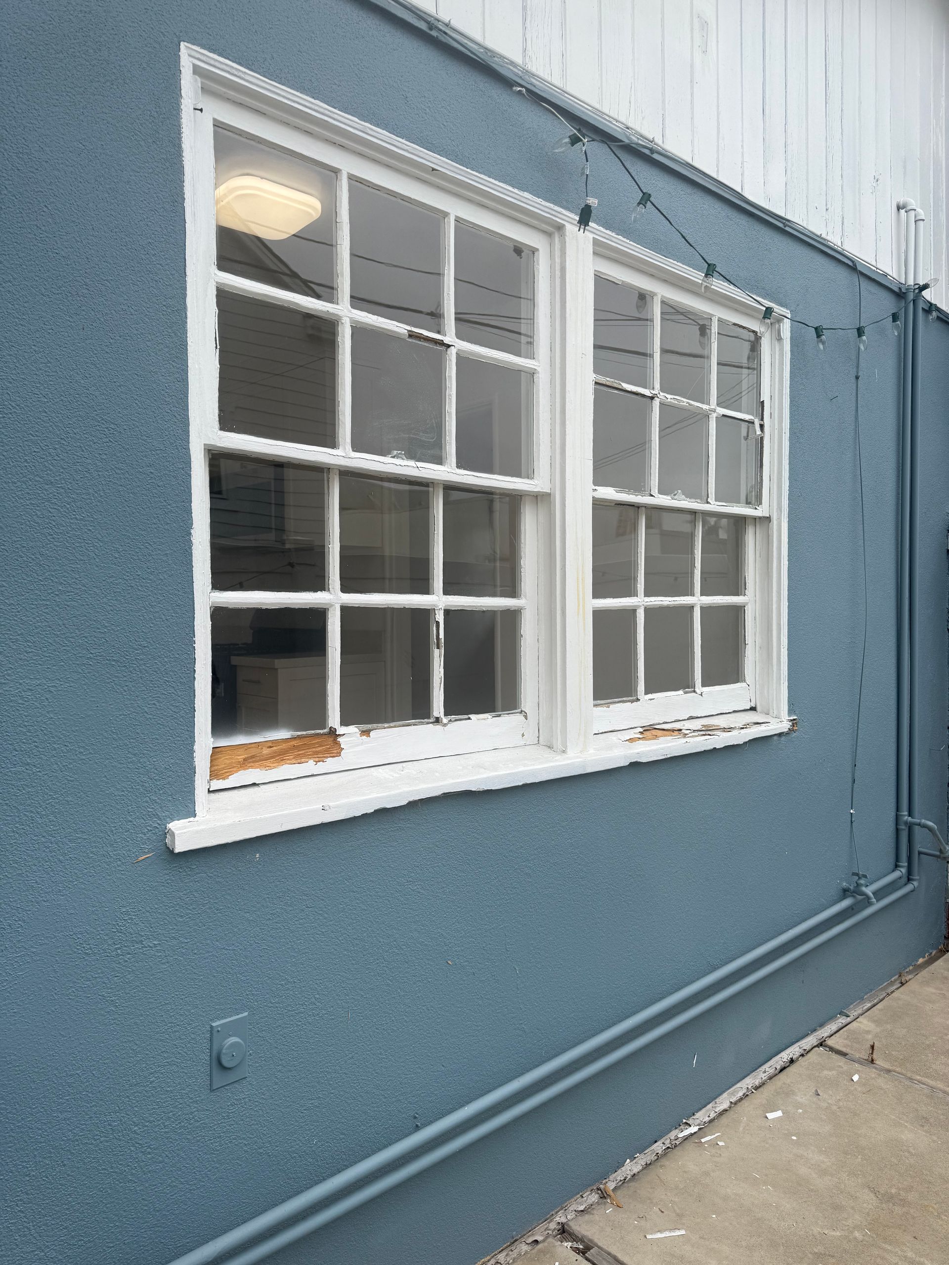 Blue exterior wall with two white-framed windows and exposed conduit beside them
