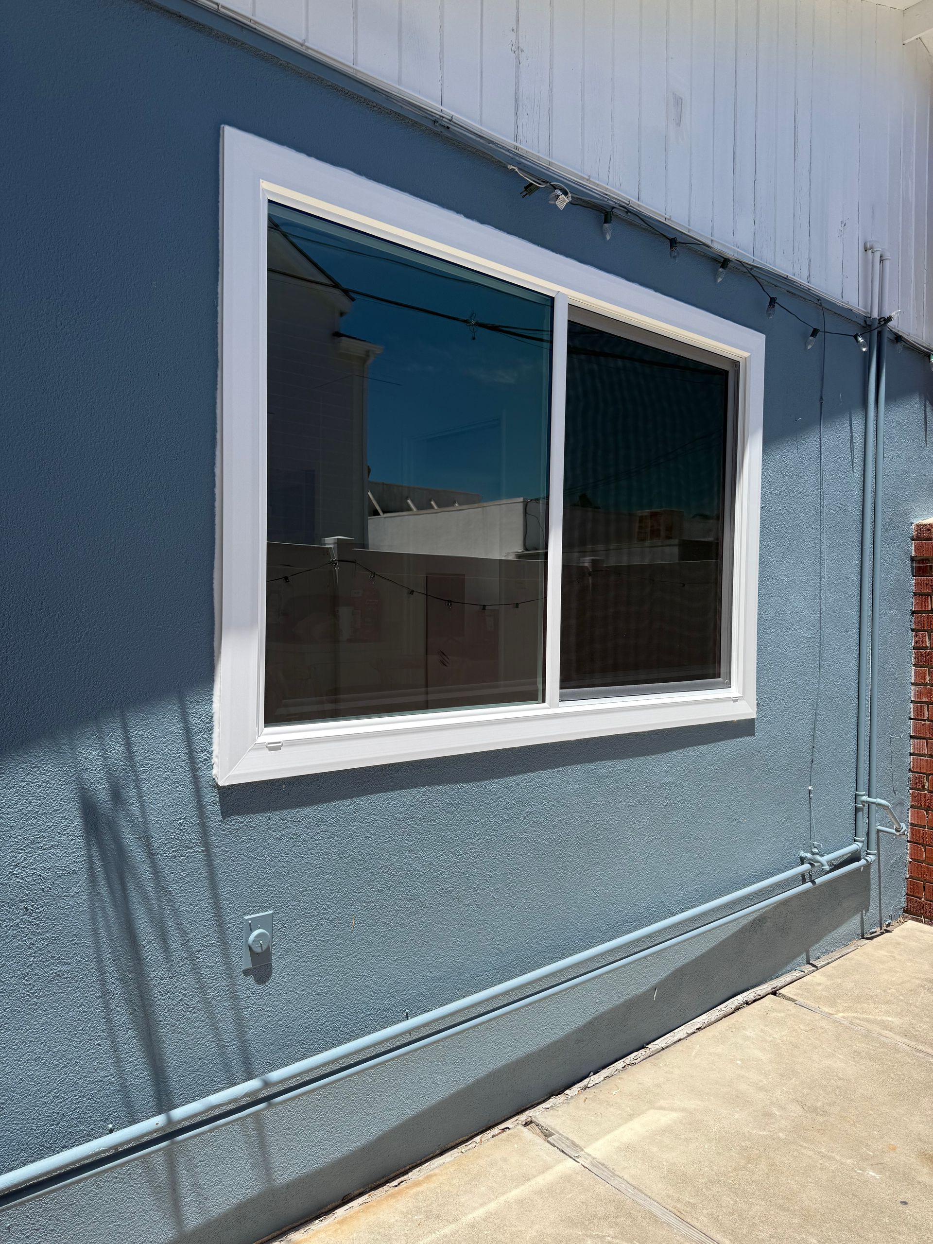 Blue building exterior with a white-framed window and sidewalk below.