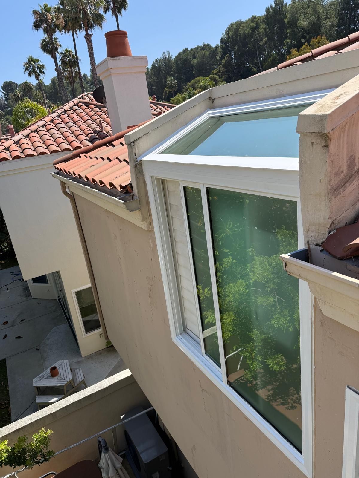 Residential rooftop with red tile roofs and a large white-framed skylight under a clear sky