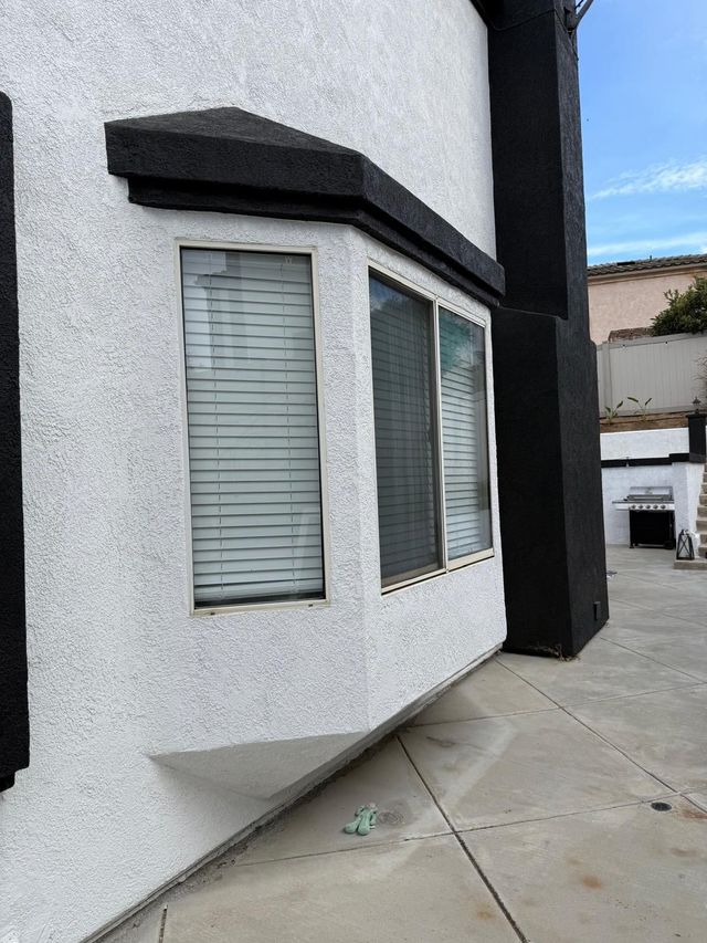 White stucco house exterior with a bay window and black trim beside a concrete walkway