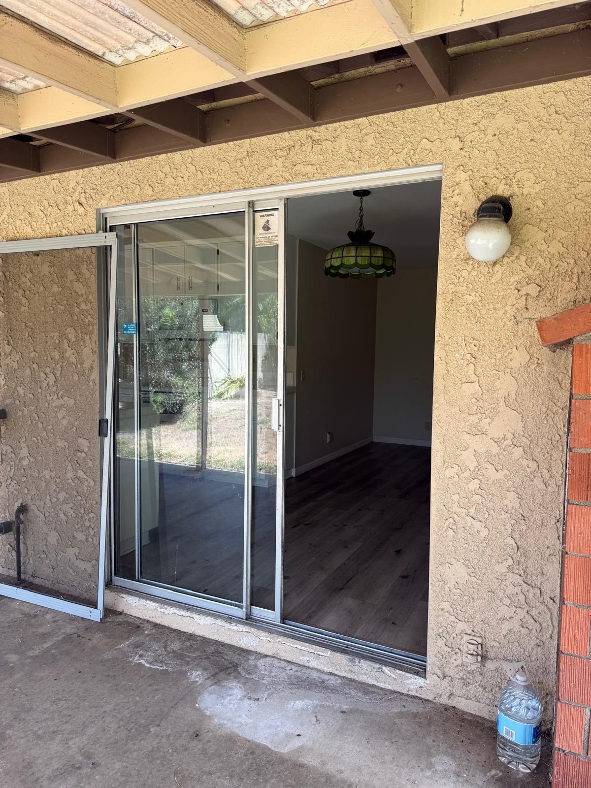 Sliding glass door opening to a small empty room with dark wood floors and a hanging light fixture