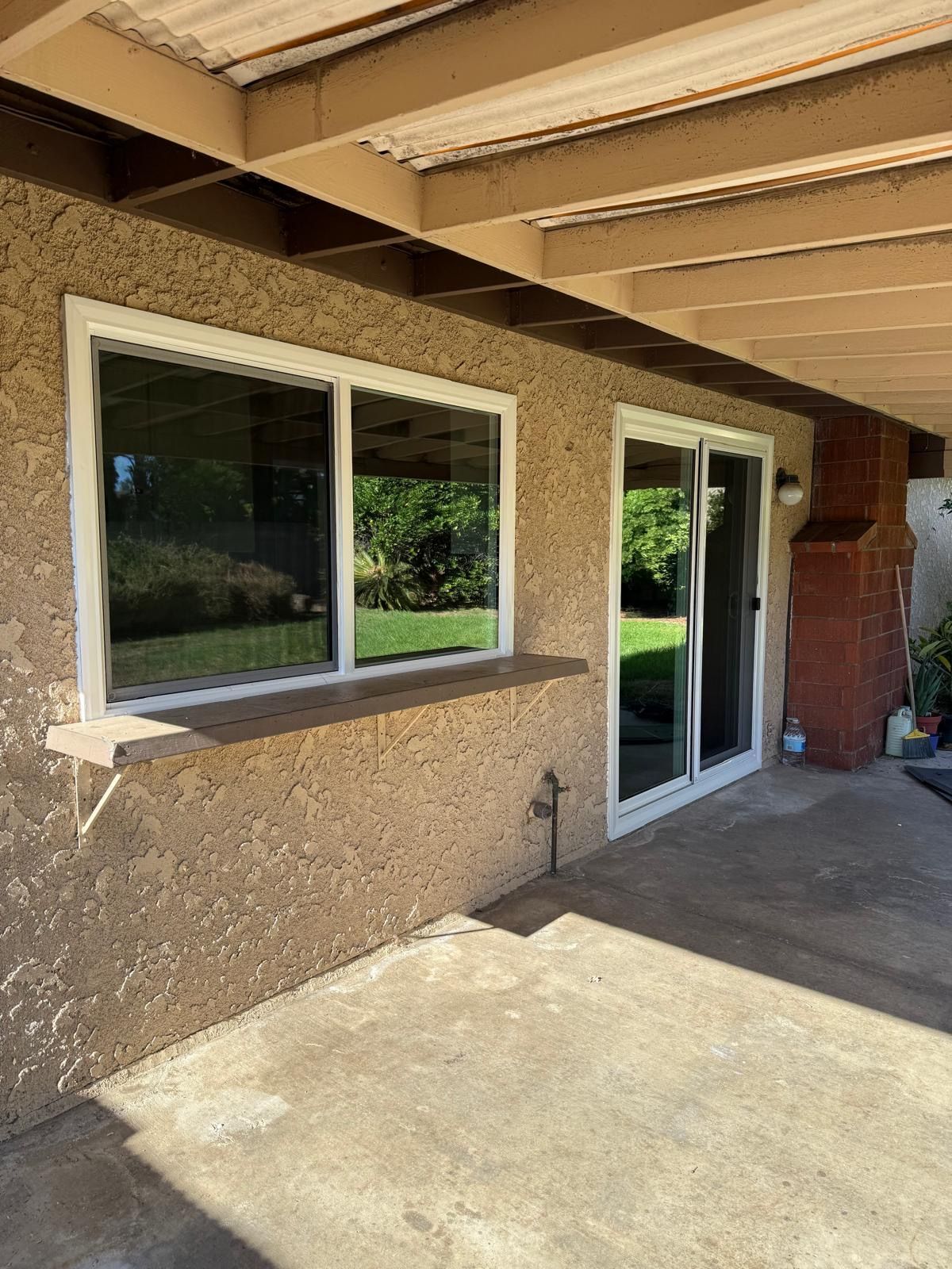 Covered patio with tan stucco wall, sliding glass door, window, and concrete floor.