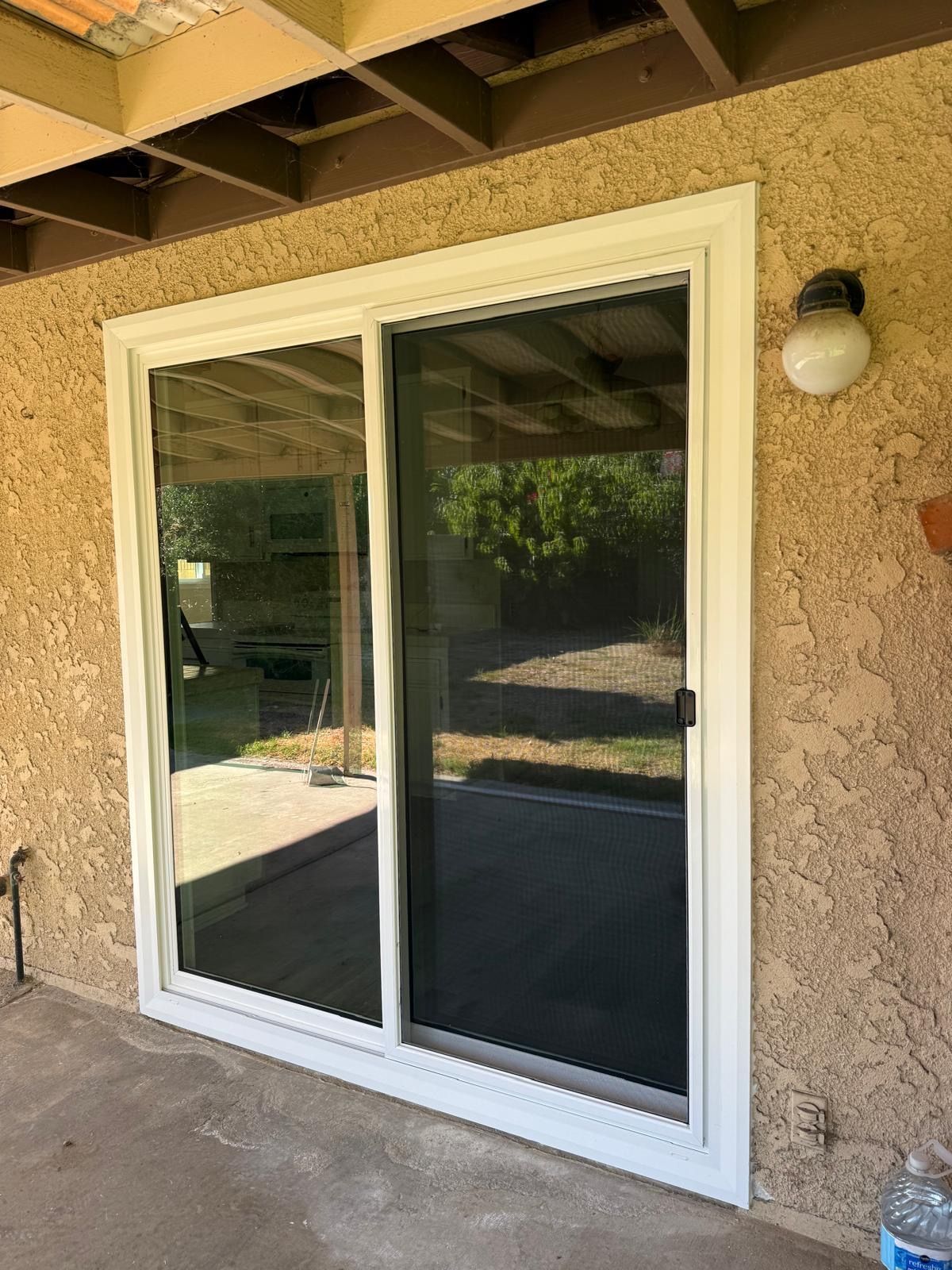 White sliding glass patio door with vertical blinds and stucco exterior wall under a covered patio.