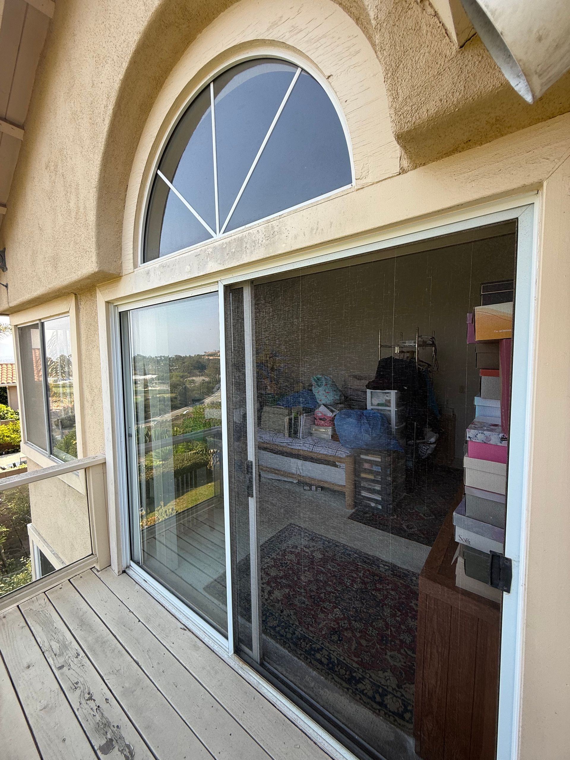 Sliding glass door beneath an arched window on a stucco house, with a wooden deck in front.