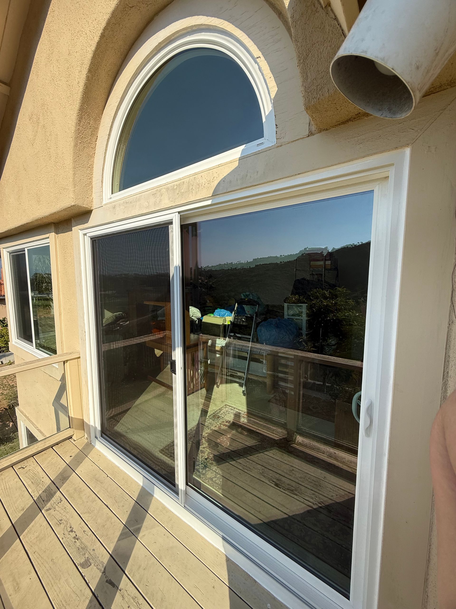 Sliding glass balcony doors under an arched window on a stucco house, with a wooden deck and mountain view.