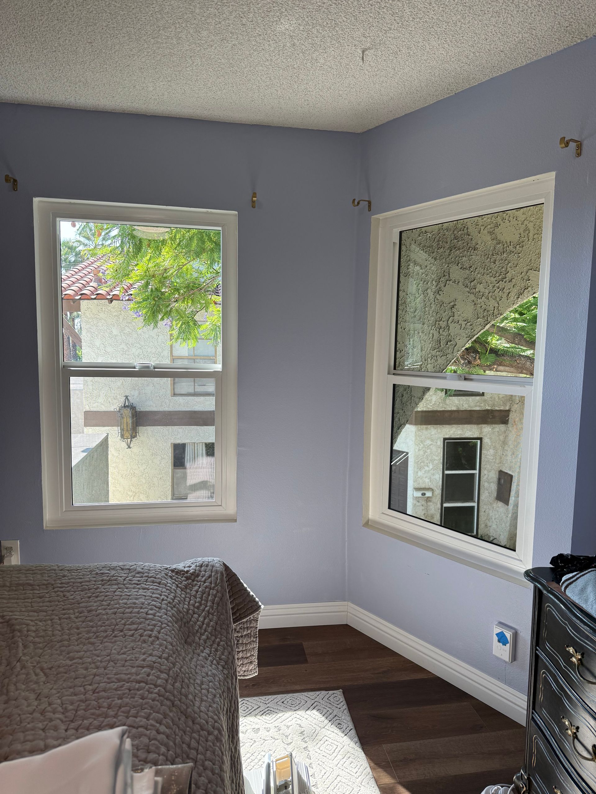 Empty room with lavender walls, two windows, and dark wood flooring.