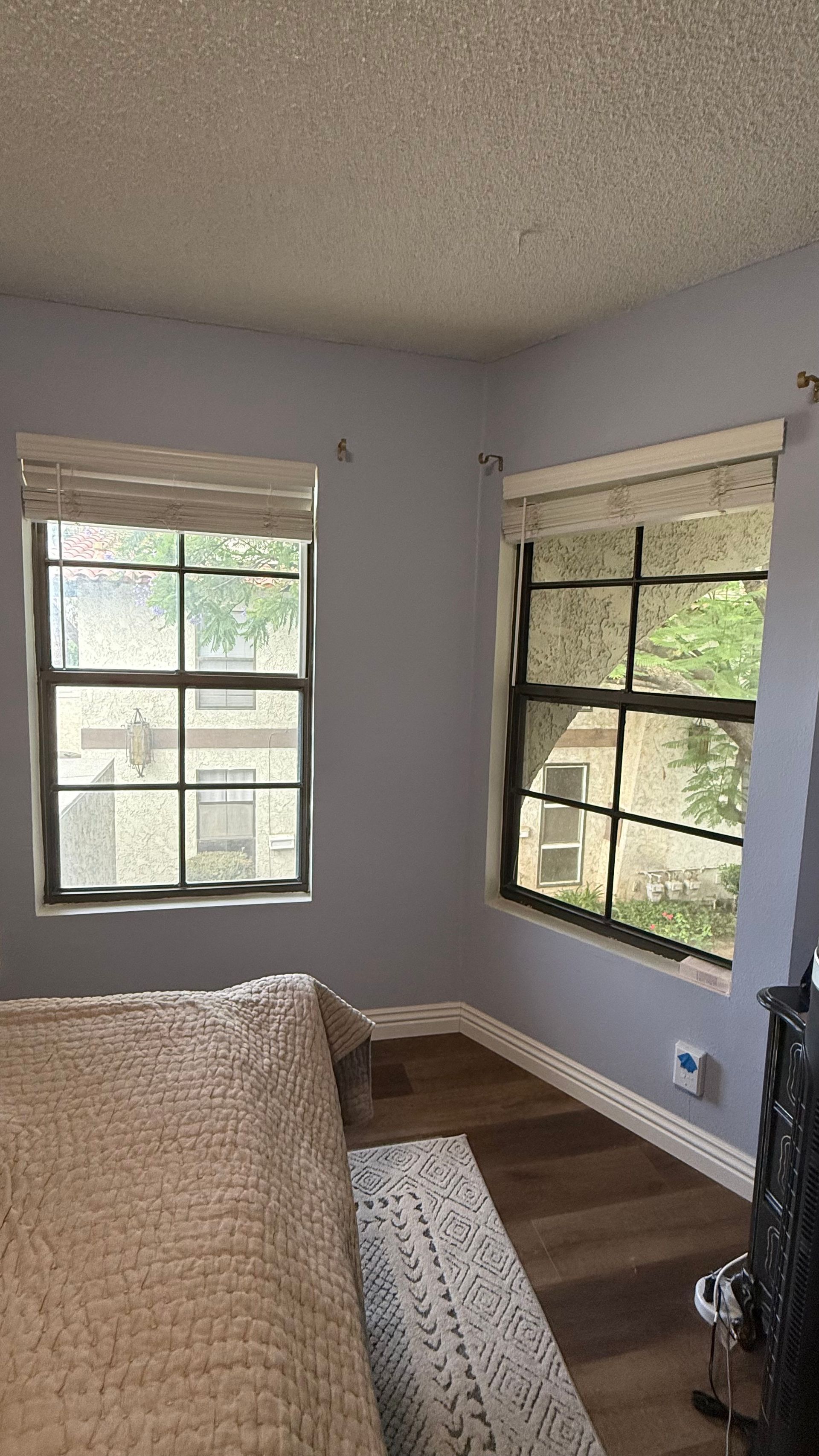 Small bedroom corner with two windows, gray walls, wood floor, and a bed in the foreground.