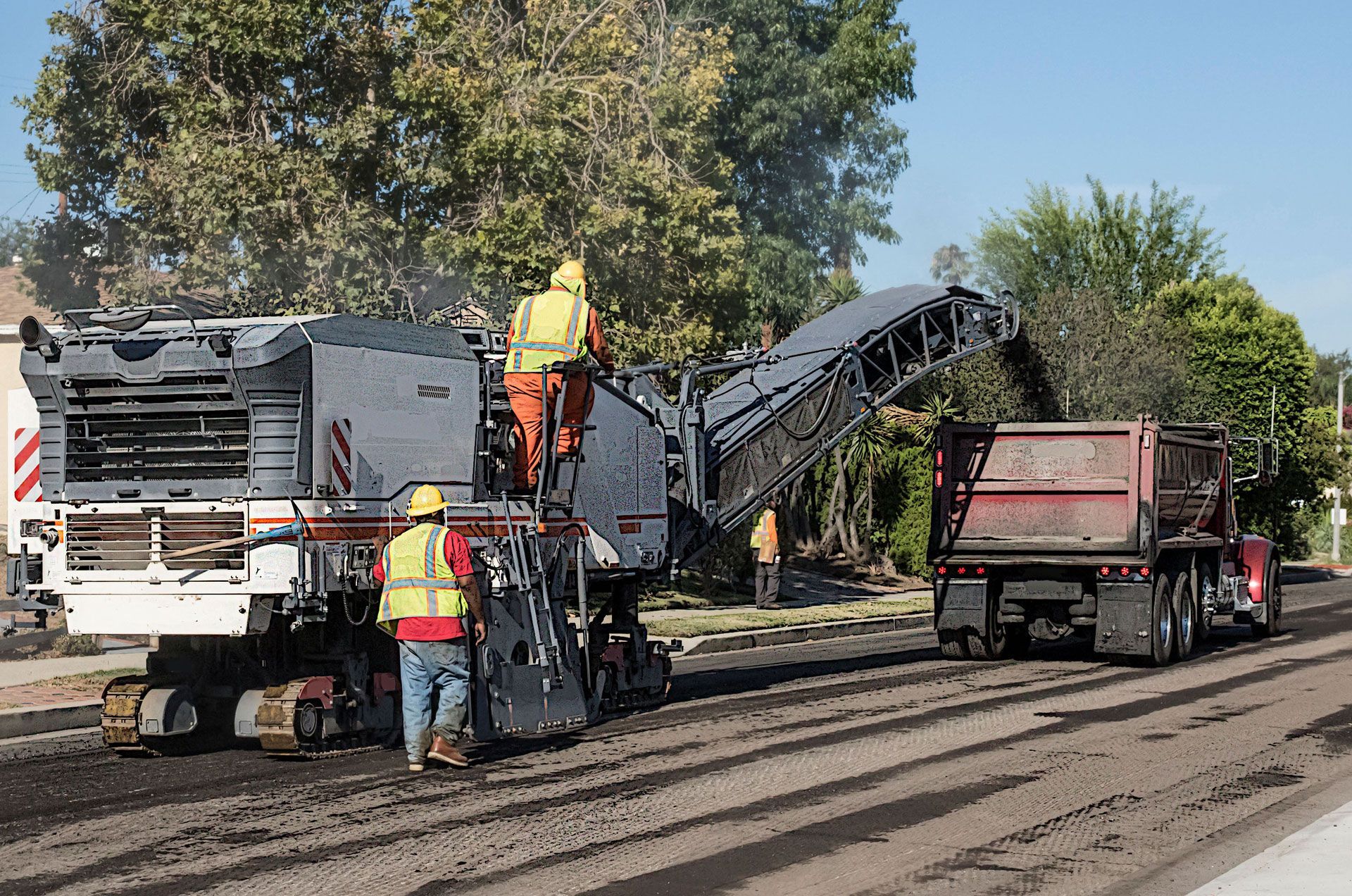 A man is standing next to a machine that is laying asphalt on a road.