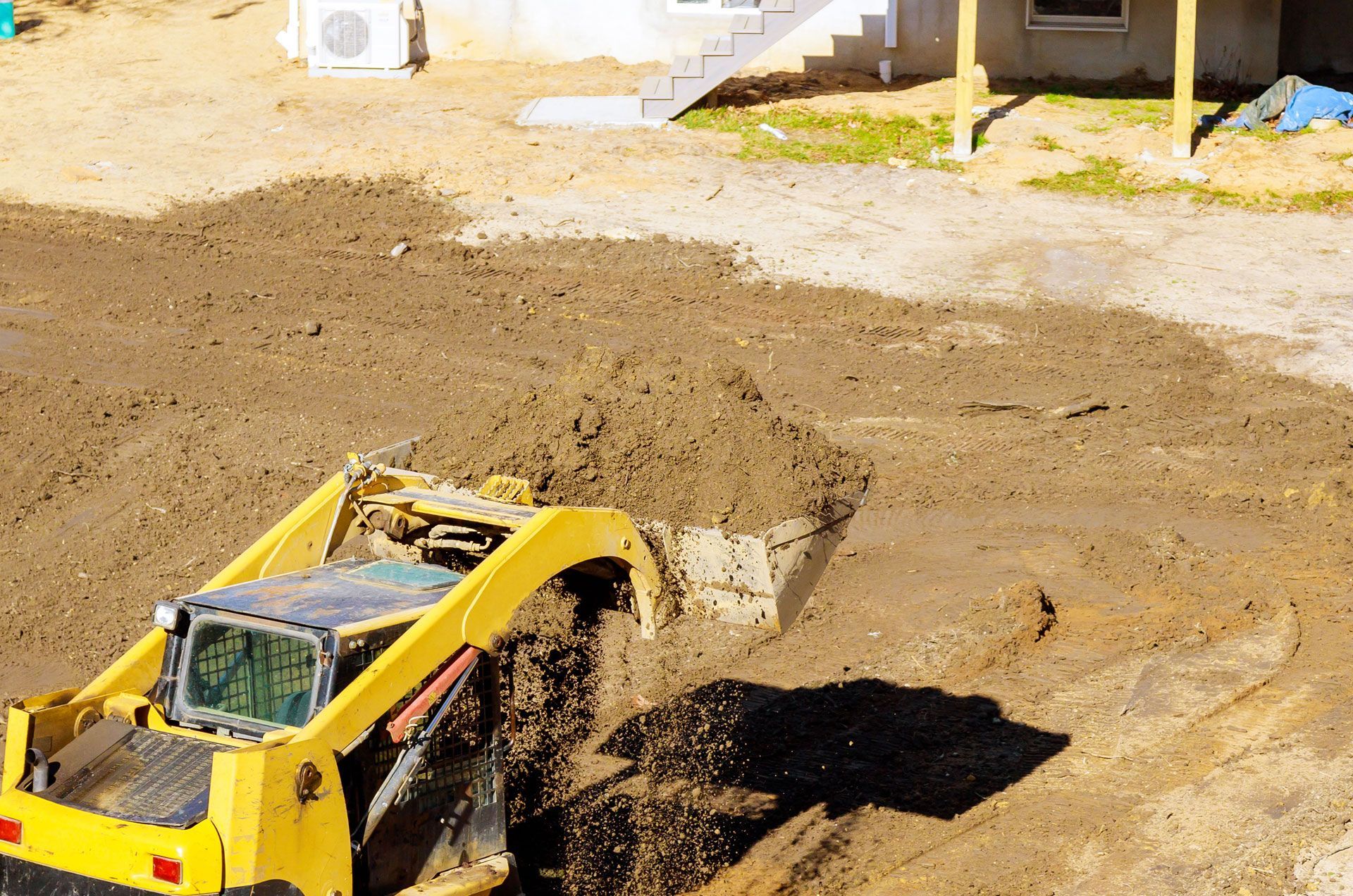 A yellow bulldozer is digging a hole in the dirt in front of a house.