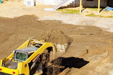 A yellow bulldozer is digging a hole in the dirt in front of a house.