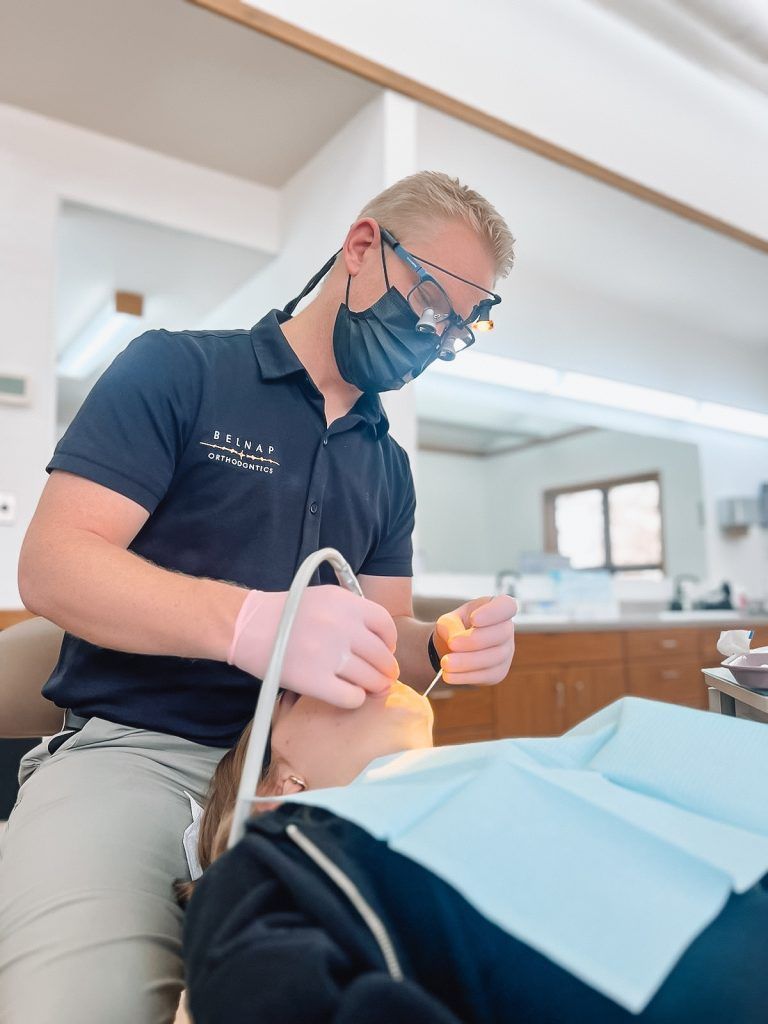 Dentist wearing a mask and gloves examining a patient in a bright clinic room
