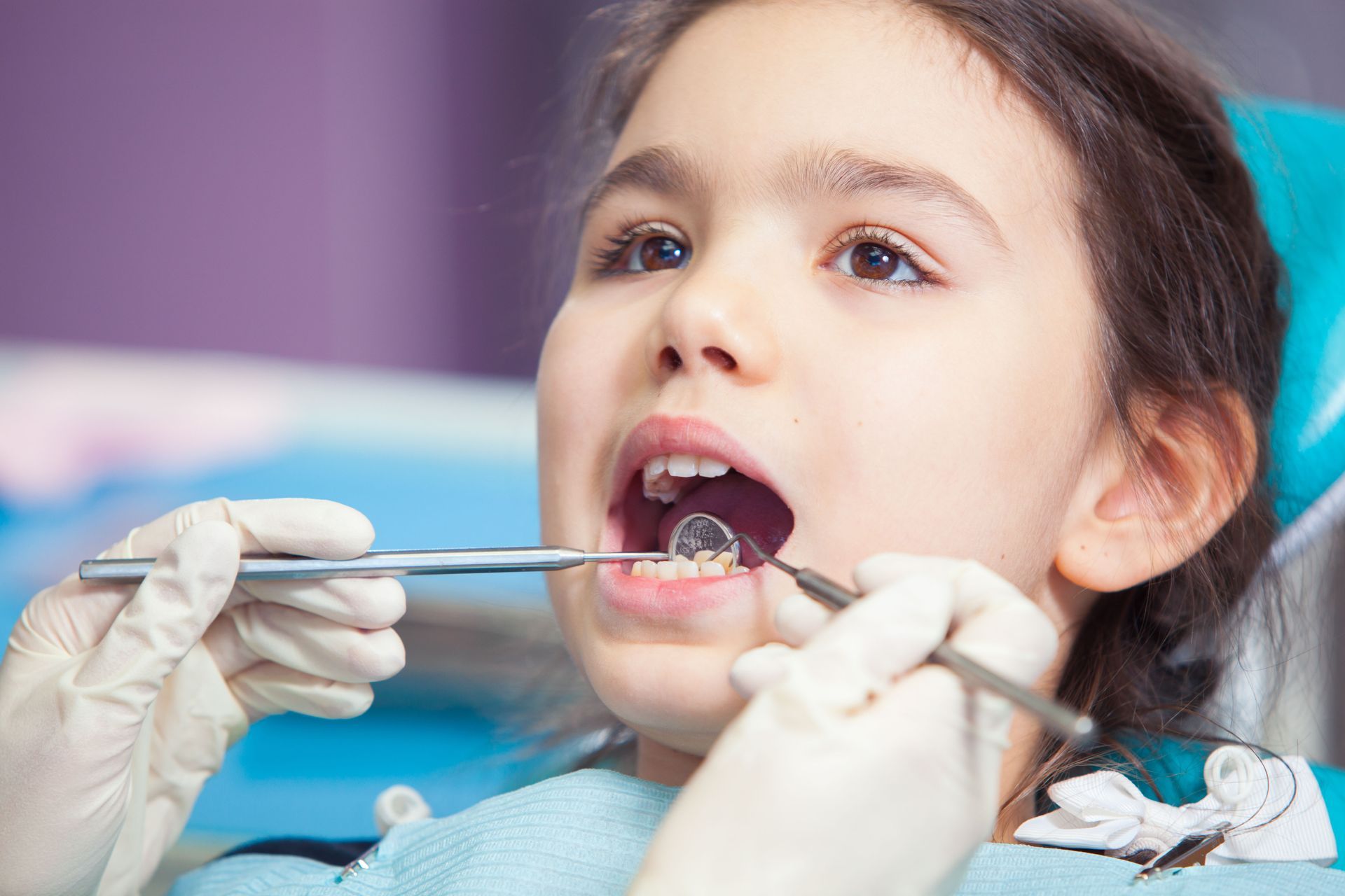 Dentist examining a child’s open mouth with dental tools and gloved hands