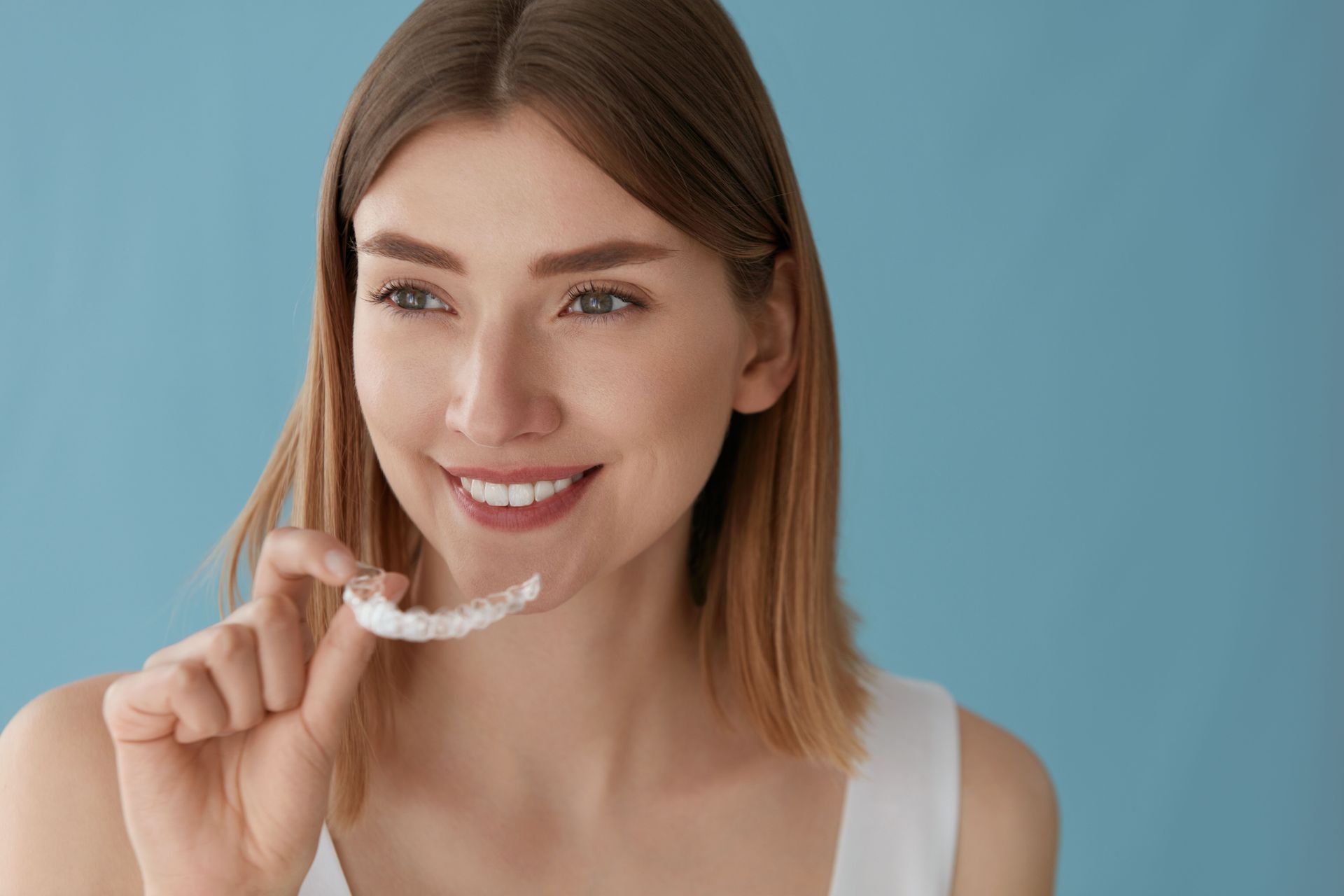 Smiling person holding a clear dental aligner against a blue background