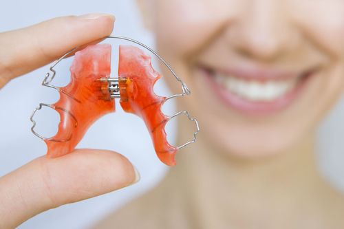 Hand holding a clear red dental retainer in front of a smiling person