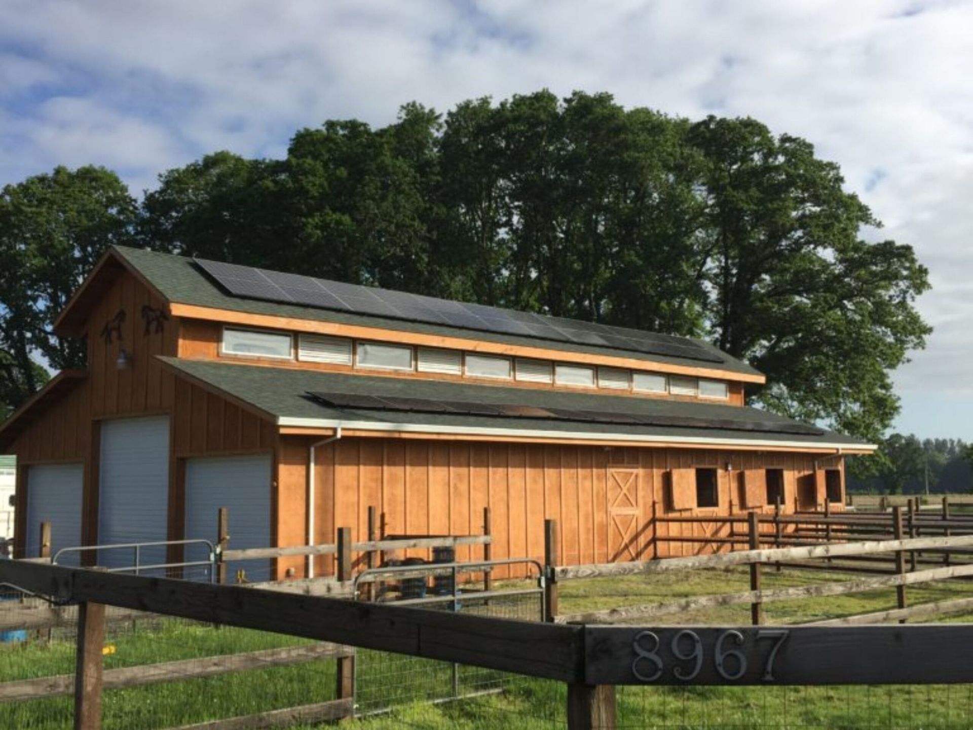 Brown barn with solar panels on roof and a wooden fence in front.