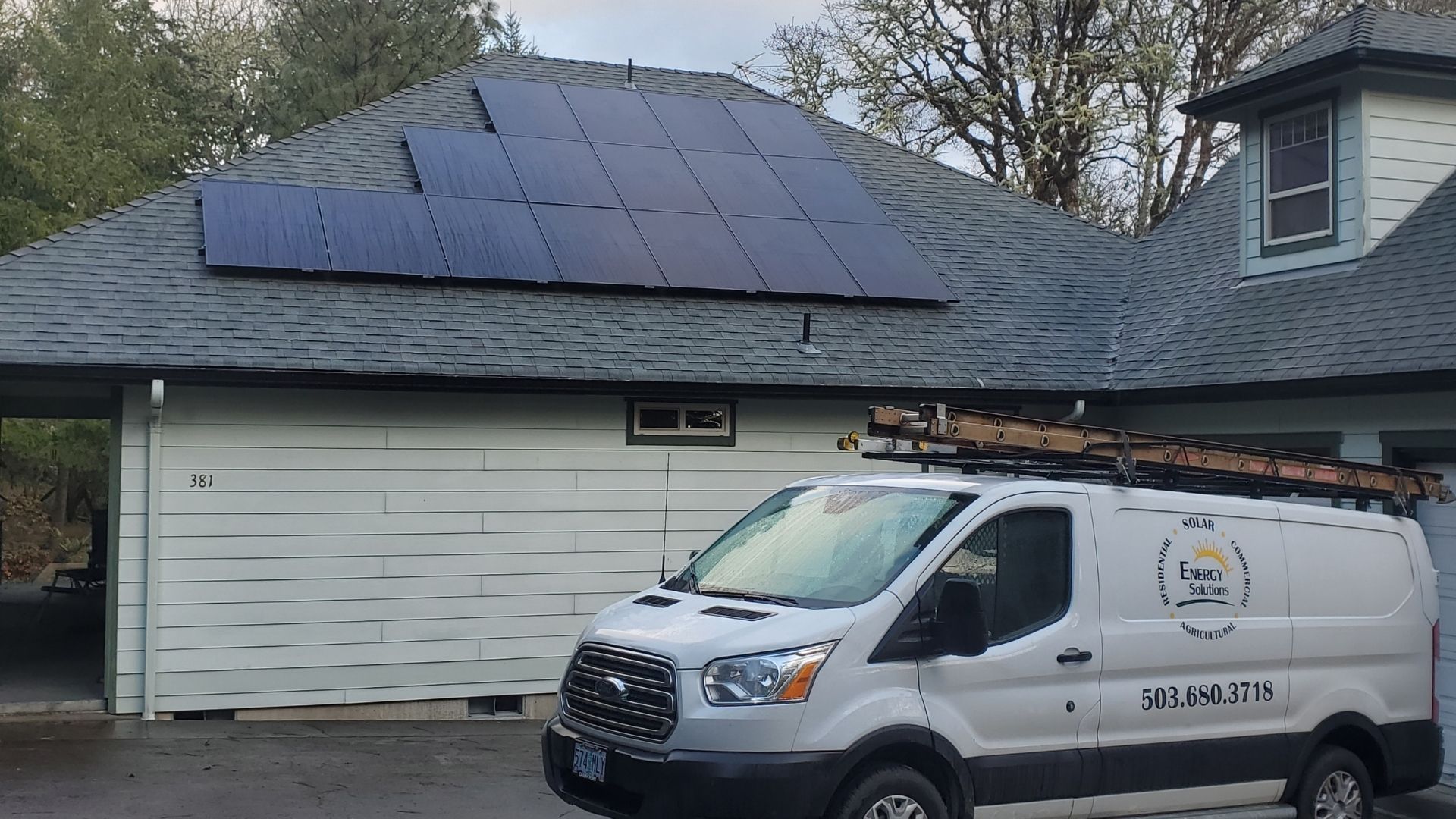Solar panels on a house roof. White van with logo in front of garage.