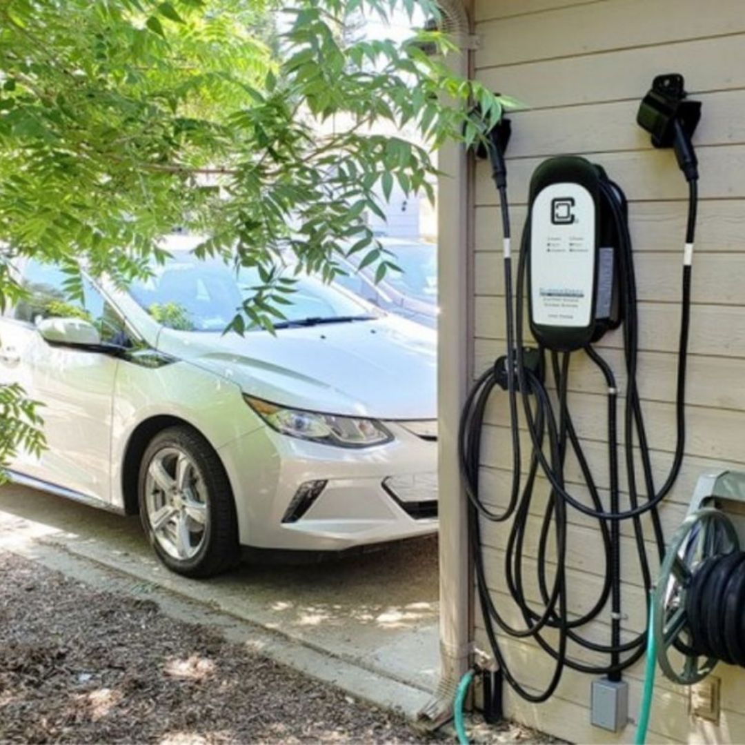 Electric car charging station on house exterior with silver car.