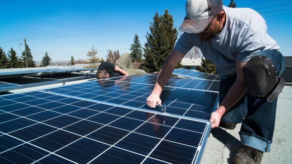Two workers installing solar panels on a roof in sunlight.