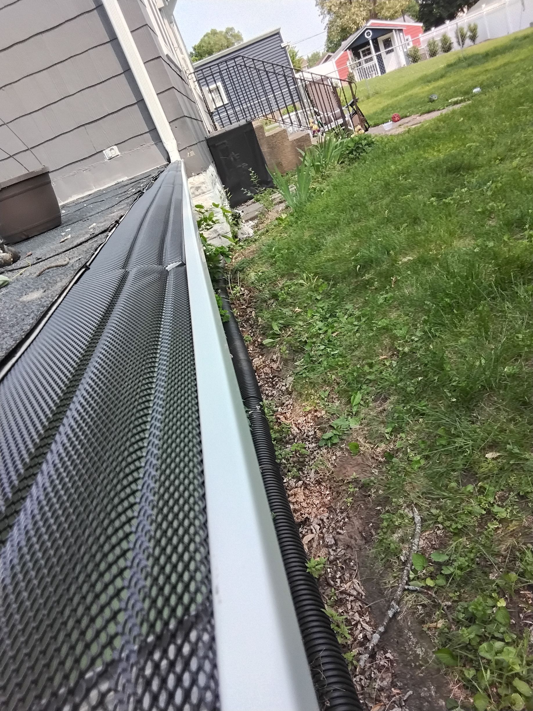 A white gutter with a black mesh on it is sitting in the grass next to a house.